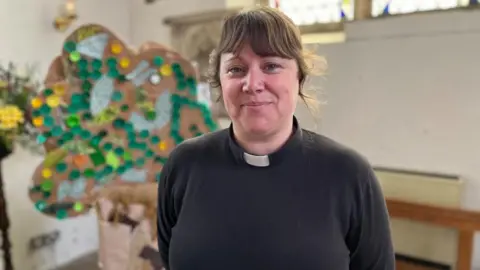 Shaun Whitmore/BBC Reverend Natalie Rees, pictured next to a sculpture of a tree