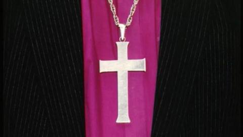 A close-up of a cross necklace worn over ecclestiastical robes