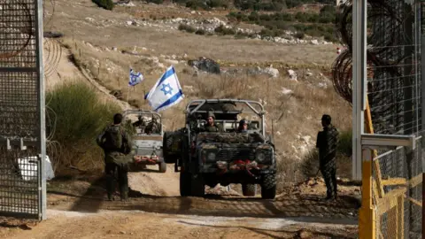 Getty Images Israeli military vehicles cross the fence as they return from the buffer zone with Syria, near the Druze village of Majdal Shams in the occupied Golan Heights on December 10, 2024