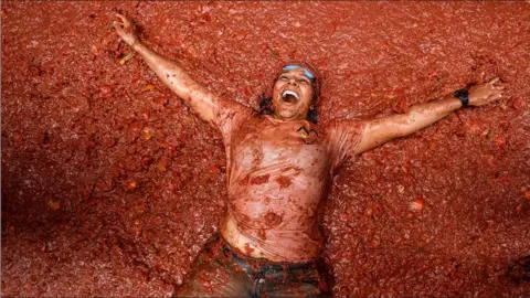 A woman lying back in a pool of tomatoes with a smile on her face 