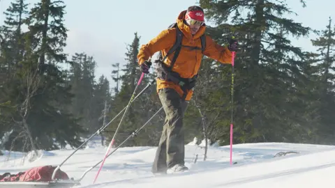 Jonny Huntington, the former GB para-athlete, hiking up a ski slope wearing protective winter gear and carrying his kit behind him.