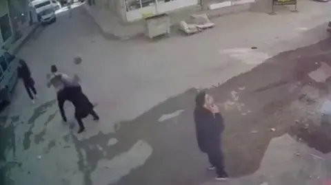 People look around in street as masonry falls to the ground