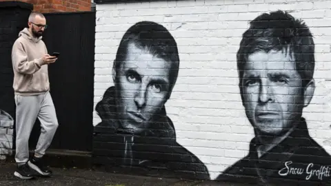 Man on phone walks past mural of Liam and Noel Gallagher