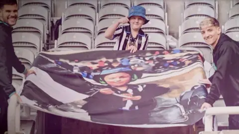 Tyler standing proudly in St James' Park stands with the flag of himself