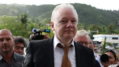 Julian Assange arrives at court in the Northern Mariana Islands surrounded by people