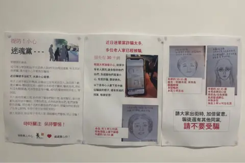 Printed posters tacked onto a wall, warn about the blessing scam with sketches of suspects.