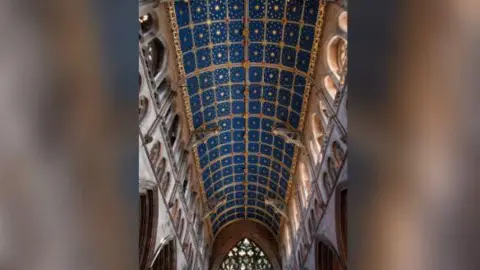 Getty Images The vaulted ceiling at Carlisle Cathedral. It is divided into squares surrounded by a golden frame, each square features a starry, blue sky.