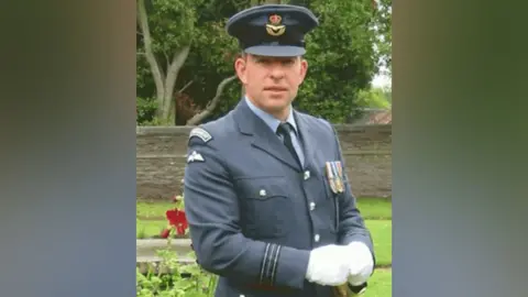 An image of Andy Williams in his dark blue RAF uniform, with an RAP cap and white gloves. A garden is seen in the background.