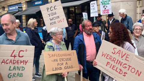 A number of people holding placards with messages such as "Save Werrington Fields", and "PCC you work for us!"