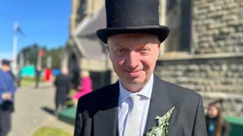 Alex Allinson smiling wearing a black suit and top hat