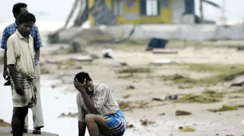 Indian men stand exhausted after searching for missing relatives at Silver Beach in Cuddalore, some 185 kms south of Madras, 27 December 2004