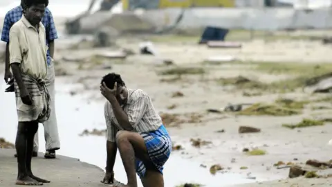 AFP Indian men stand exhausetd after searching for missing relatives at Silver Beach in Cuddalore, some 185 kms south of Madras, 27 December 2004, after tidal waves hit the region. 