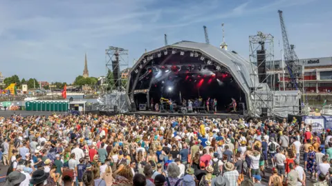 A large crowd watching a band performing on the Harbour Festival's main stage during the day