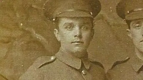 A sepia close-up photo of Albert Dove who is wearing a military uniform with a hat. Another man can be seen on the right but has been cropped out of the photo.