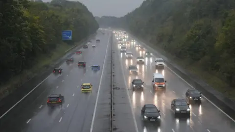 A motorway, with oncoming traffic and traffic heading away, side by side, it is a wet December day