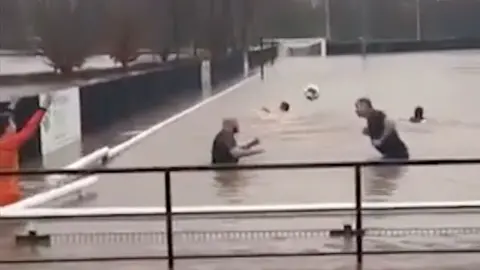 Players heading football in flooded pitch