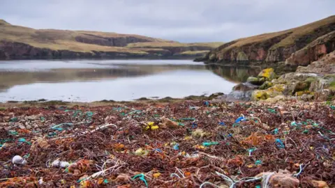 A calm loch surrounded by hills. In the foreground are lots of discarded fishing nets in a variety of colours