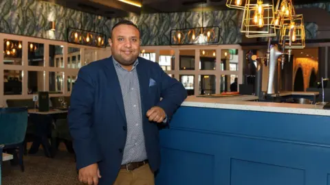 Gaurav Barot Gaurav Barot in his restaurant in Newry.  He has short, dark hair and is wearing a navy blazer, a blue patterned shirt and beige trousers with a brown belt.  