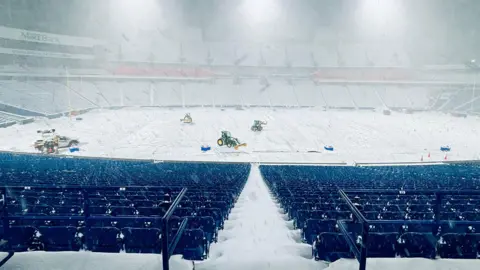 Plows on an NFL stadium work to remove snow