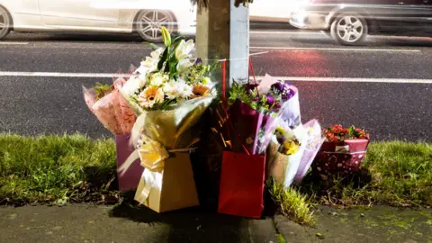 floral tributes against a pole beside a road in Dublin