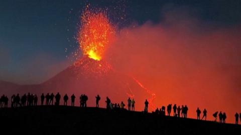 erupting volcano with people silhouetted in foreground