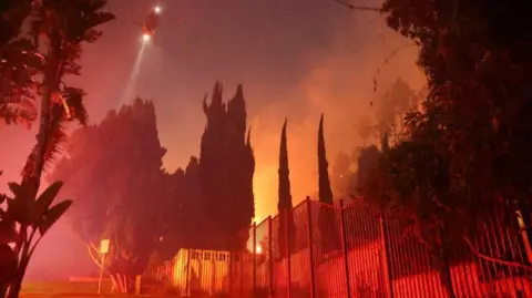 A helicopter flies, as smoke rises from the Sunset Fire