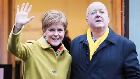 Nicola Sturgeon and Peter Murrell standing side by side in overcoats.