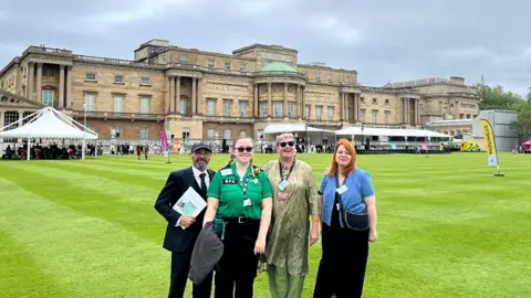 Hafwen Clarke Hafwen Clarke on the lawn at Buckingham Palace alongside three other people