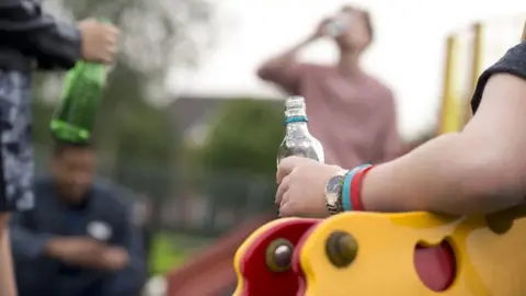 People sat on children's park equipment holding bottles