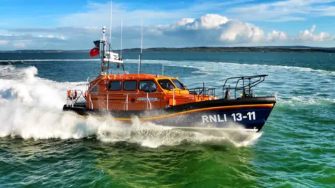 An orange and blue Shannon class RNLI lifeboat cutting through the waves on the sea during a call-out.