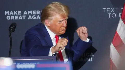 Donald Trump, wearing a blue suit and red tie, dances as he leaves the stage during a campaign rally New Hampshire