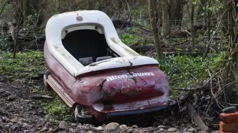 A purple and white theme park water flume 'boat' laid in light undergrowth