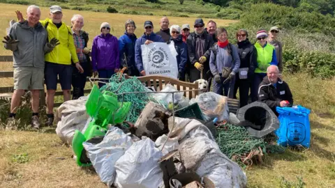 Plastic Free West Somerset Volunteers stood in a field with a large pile of debris found on the beach