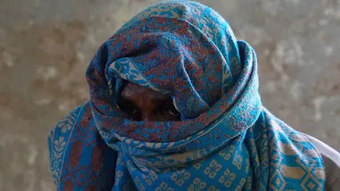 A fisherman-turned-pirate looking directly at the camera through a blue patterned scarf wrapped around his head only allowing his eyes to peep through - Eldoret, Somalia