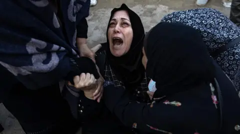 Palestinians mourn next to the bodies of their relatives who were killed in an Israeli air strike, west of Khan Younis, in the southern Gaza Strip, on 12 December 2024