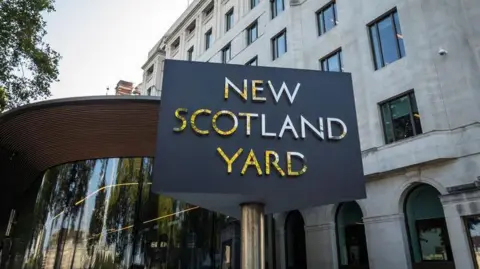 Getty Images Sign for New Scotland Yard in front of a modern building with large windows and architectural details, under a clear sky.