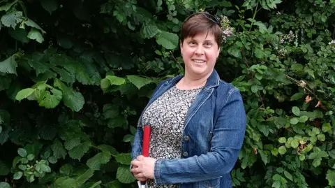 Louise Plunkett stands in front of a hedge, holding her cane.