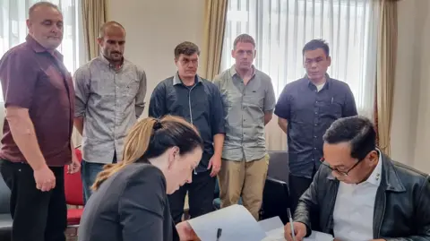 'Bali Nine' (L-R, background) Martin Eric Stephens, Michael William Czugaj, Scott Anthony Rush, Mathew James Norman and Si Yi Chen inside a room in Bali International Airport during a handover process for their return