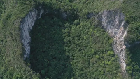 Aerial photo of a sinkhole dropping away in the middle of the forest in China's Guangxi province