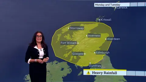 Weather presenter Judith Ralston, wearing a black and white dress, stands in front of a map of Scotland with a large yellow rainfall patch highlighting an area where heavy rain is expected.