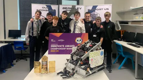 BBC Eight Berkeley Green UTC pupils stand together in a classroom between their robot on the table