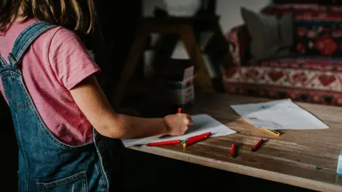 A little girl with brown hair draws on a piece of paper