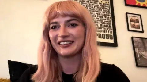 Olivia Bridge, a woman with light blond pink hair smiles and looks at the camera  