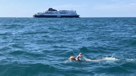 A child in the water, with a DFDS ferry in the background