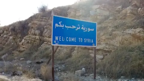 Blue road sign which has 'welcome to Syria' written on it