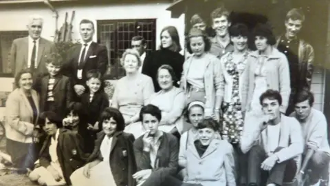 Amicale Hery Shilbottle Association A black and white photo of a group of different age - with the children sitting on the ground