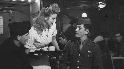 Getty Images A black and white photo of an English volunteer waitress waiting on club members at Rainbow Corner, the American Serviceman's Club off Piccadilly Circus. 