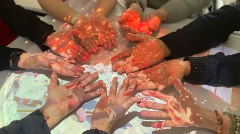 Residents of a care home hold out the palms of their hands in a circle while interacting with light technology