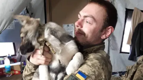 Tindal-Draper family handout Callum Tindal-Draper in a makeshift army barracks holding a puppy while out in Ukraine.