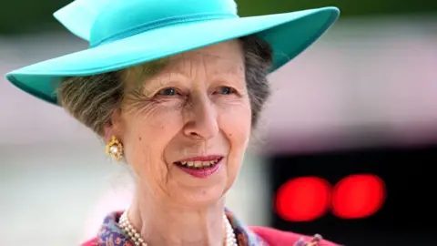 PA  Princess Anne smiling, wearing gold earrings and a turquoise hat